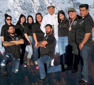 A group of friends posing in front of a mountain backdrop with a man in a white naval uniform.