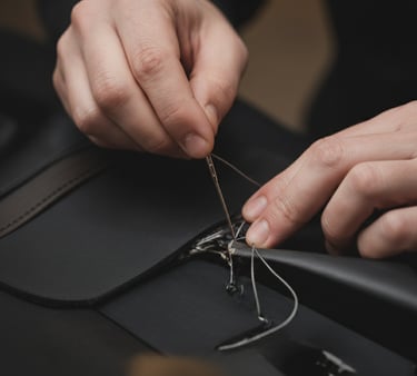 Close-up of hands sewing black leather material with a needle.
