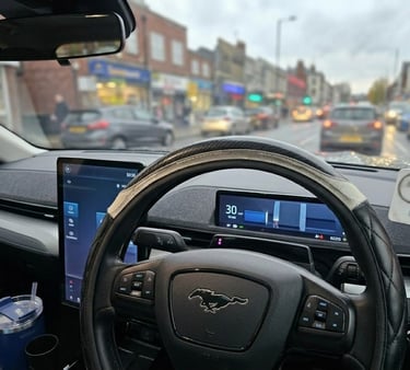 Interior view of a Ford Mustang Mach-E dashboard showing the steering wheel and digital displays in city traffic.