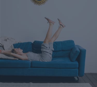 Mujer relajada sobre sofá azul en salón minimalista, transmitiendo confort y bienestar en el hogar — imagen representativa de