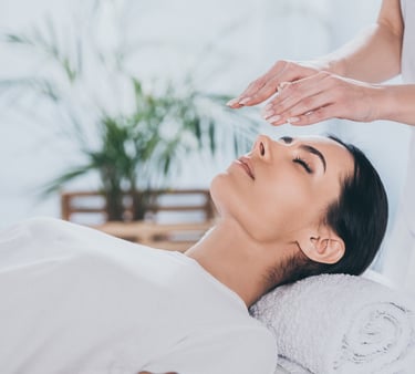 Reiki practitioner performing energy healing over a relaxed woman at a wellness spa.