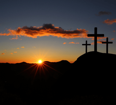 The sun rises over a dark hill with three crosses on it.
