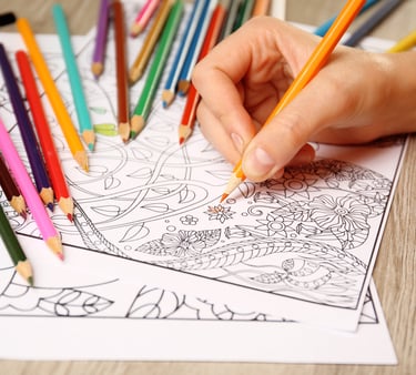 A person coloring an intricate floral adult coloring book page with vibrant colored pencils.