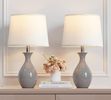 Pair of gray ceramic table lamps with white drum shades on a console table.