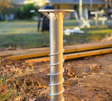 A galvanized steel ground screw pile installed in dirt for a backyard deck foundation.