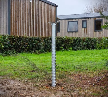 Galvanized steel ground screw foundation installed in a grassy yard for eco-friendly building construction.