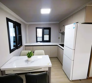 Modern minimalist kitchen with white cabinets, marble dining table, and large white refrigerator.