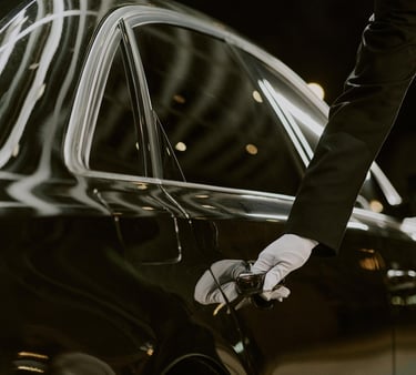 A chauffeur in white gloves opening the door of a black luxury car for executive transport.VIREMONT 
