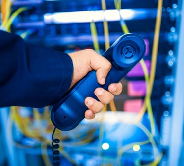 Person holding a phone behind a network rack, representing IT support and remote troubleshooting services