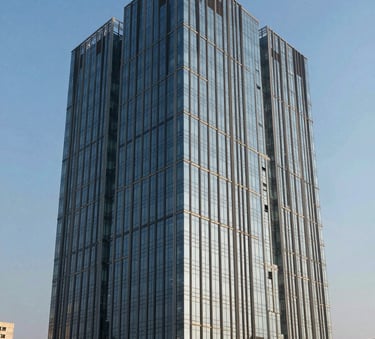 A contemporary commercial office building in a Noida business park, featuring glass walls and modern architecture under a clear blue sky, South Asian urban setting.