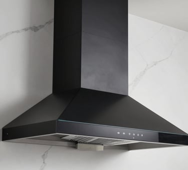 A side-angle professional photograph of a modern black glass kitchen chimney being installed on a white marble wall. The lighting is crisp, highlighting the premium finish of the unit.