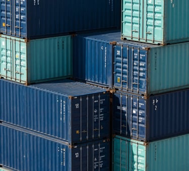 A clean, high-angle architectural photograph of neatly stacked shipping containers in shades of dark blue and teal at a modern North American shipping port, bright daylight, sharp focus on the textures of the steel.