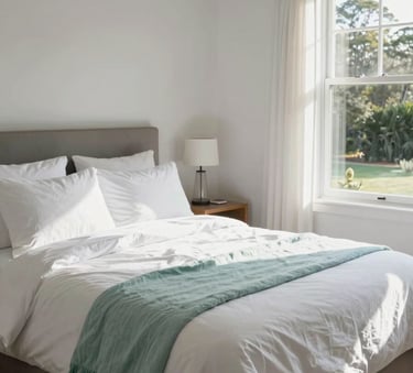 A beautifully staged Australian holiday home bedroom with crisp white linens and a light teal throw, sun streaming through the window, pristine and fresh atmosphere.