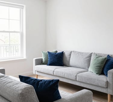 A bright and airy modern Airbnb living room in Saint-Denis, featuring light grey furniture and soft white walls. The composition is clean and minimalist, showing a space that has just been professionally cleaned. Natural light filters through large windows, highlighting the lack of dust. Colors include midnight blue pillows and sage green accents.