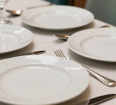 A close-up photograph of a set of pristine white dinner plates and polished silverware in a high-end Marrakech restaurant. The lighting is soft and warm, highlighting the cleanliness and professionalism. Subtle hints of Dark Teal and Soft Sage appear in the background decor.