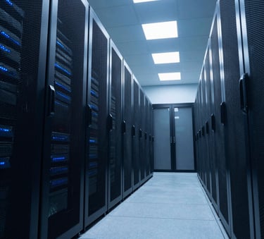 A low-angle, wide shot of a futuristic North American data center hallway with rows of servers. The atmosphere is professional and clean, with cool sky blue and medium navy lighting reflecting off the metallic surfaces.