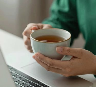 A close-up, calming shot of a person's hands holding a ceramic cup of tea near a laptop, signifying a comfortable home therapy environment. Soft lighting, professional and empathetic mood, featuring accents of #5DA399 and #A7D9D3 in the room decor.