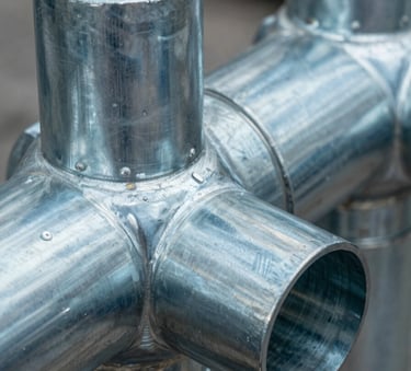 A sharp, detailed macro photograph of industrial galvanized steel duct joints, highlighting precision manufacturing and high-quality materials. The metal surface has a cool steel blue sheen with soft grayish blue highlights.