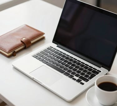 A professional workplace setting in North American / US showing a high-end laptop on a white desk next to a leather notebook and a cup of coffee, bright and airy lighting to convey clarity and modern professionalism.