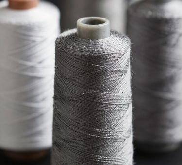 A high-detail close-up of industrial-grade sewing thread spools in professional tones like #5B7B7C. The lighting is sharp and focused, emphasizing the durability and premium quality of the thread material.