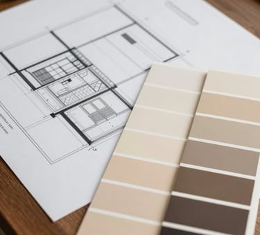 A designer's desk in a North American / US home office, showing architectural facade plans and high-quality paint swatches in warm beige and deep charcoal.