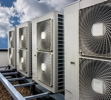 A row of industrial air conditioning units installed on a gravel rooftop under a blue sky.