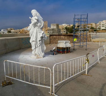 White marble statue of the Virgin Mary and child at a coastal construction site with scaffolding.