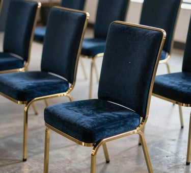 A collection of modern dark blue velvet chairs with gold metal legs, arranged in a clean, sophisticated North American event space with natural light.