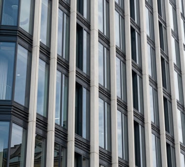 A close-up photograph of modern architectural glass and steel cladding on a sustainable building in a French / European urban district. The lighting is crisp, reflecting steel blue and off-white tones.