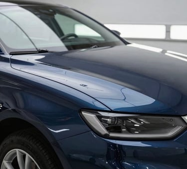 Close-up of a professional detailing a high-end car exterior in a clean North American garage, focused lighting on polished surfaces with deep navy and slate blue tones.
