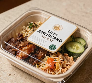 A close-up photograph of a premium, elegantly packaged ready-to-eat gourmet meal on a beige stone surface. The lighting is warm and natural, highlighting the fresh textures of the food. Latinoamericano setting.