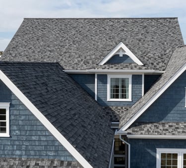 A wide-angle shot of a beautiful North American suburban home featuring a newly installed dark gray architectural shingle roof and slate blue siding, clean lines, bright daylight, professional craftsmanship.