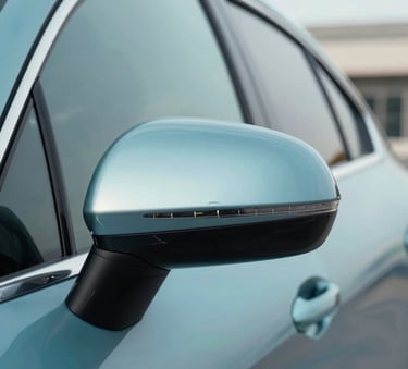 Close-up of a high-end car's side mirror and door, polished to a mirror-like finish, reflecting a clean modern building and a clear sky, colors featuring #3E6C8F and #EBF5F9 tones, professional automotive photography style.