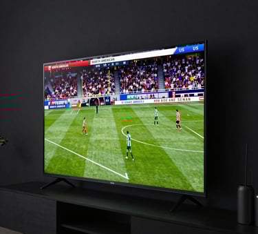 A side view of a large flat-screen television mounted on a dark wall showing a vibrant sports broadcast in a North American / US living room with ambient evening lighting.