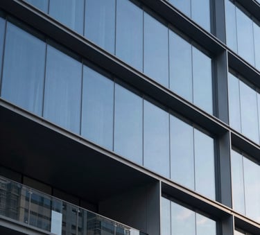A high-end, minimalist architectural detail of a modern steel and glass building in a North American city. Sharp angles, soft morning light, muted steel blue and deep charcoal tones. Luxury professional aesthetic, extremely clean composition.