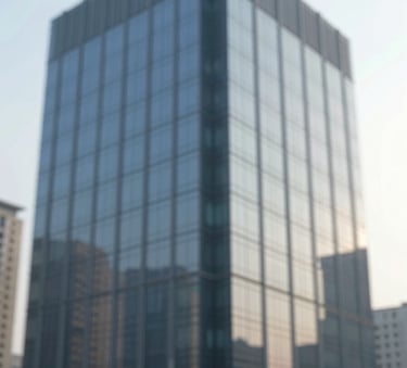 Modern office building exterior with reflective glass, clean lines, representing corporate stability and professional management, dominated by #3A6076 and #94B0C7 tones.