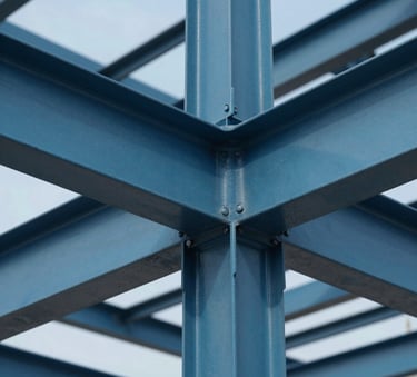 A close-up, high-detail photograph of a complex industrial steel structure with perfect joints, shot during a clear day with professional architectural lighting. The scene features the brand colors #345D7E and #0B1C2E in the metal and sky, projecting technical mastery and reliability.