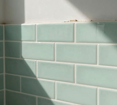 A close-up photograph of professional tile replacement in a modern North American bathroom, showing clean white grout lines and soft mint green subway tiles under bright natural light.