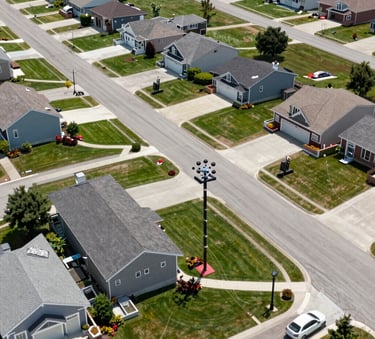 A high-altitude aerial photograph of a clean, modern North American suburban neighborhood with fiber optic infrastructure being installed, bright daylight, sharp focus on residential streets and green spaces.