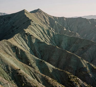 A wide-angle landscape photograph of a sun-drenched mountain ridge in North America, symbolizing strength and endurance, with soft sage green and charcoal tones in the early morning light.