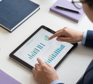 A top-down view of a clean workspace where a professional in business attire is analyzing data on a tablet. The scene is lit with bright, natural light and features accents of Midnight Navy and Soft Periwinkle in the stationery.