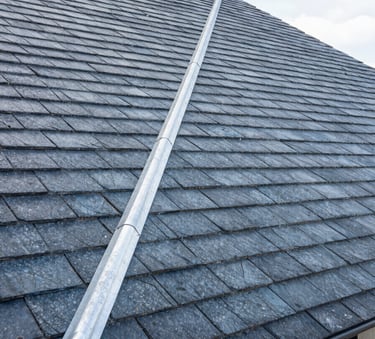 Architectural photography of a clean, modern roof with grey blue slate tiles and perfectly installed zinc flashing, high-contrast daylight, Western European / French residence.
