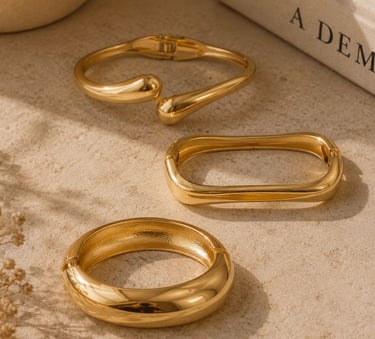 Gold statement bracelets styled on a beige surface with warm sunlight and neutral decor.