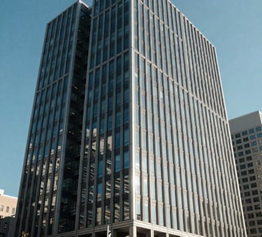 The exterior of a modern, clean glass and steel office building in a North American business district under a clear blue sky, representing growth and stability.