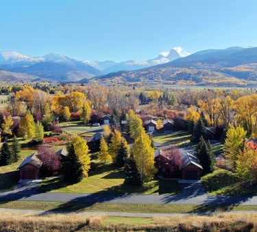 Aerial view of a mountain valley neighborhood with autumn foliage and snow-capped peaks in the background.