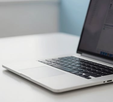 A close-up shot of a modern, silver laptop on a clean white desk in a room filled with Mist White and Soft Sky Blue accents. The lighting is bright and natural, reflecting a professional and efficient workspace.