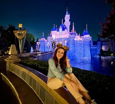 Woman sitting in front of Sleeping Beauty Castle - Disneyland after dark