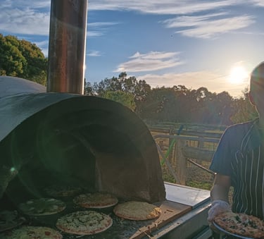 Our waiter next to a pizza oven, at a party with a sunset in the background