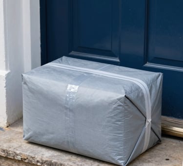 A neatly packaged parcel sitting on a modern British doorstep, crisp morning lighting, professional product photography style, using slate blue and light grey tones.