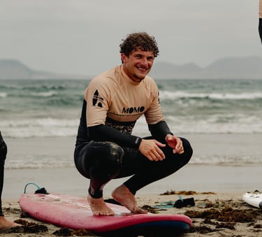 eleve de momo surf school sur sa planche entrain de sourire a la camera